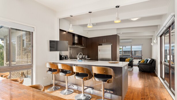 A modern kitchen with a central island, bar stools, and a dining area. - Spacious 4-bed Home 5-min From the Beach (Melbourne)