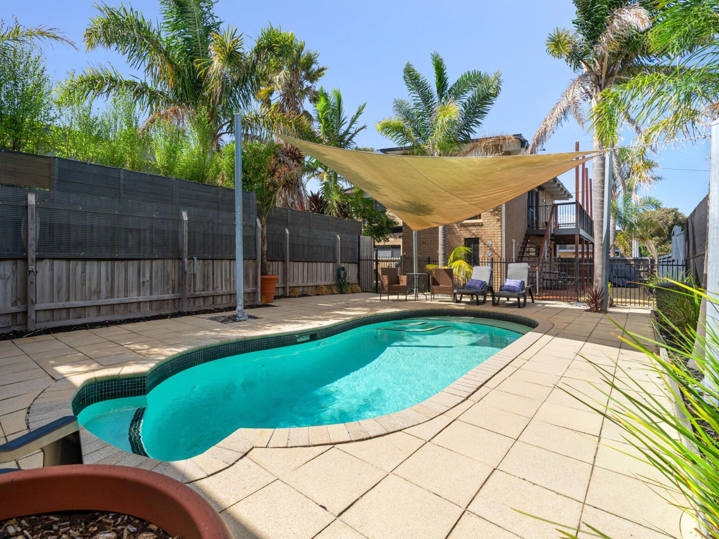 A backyard with a swimming pool, patio furniture, and a wooden fence.