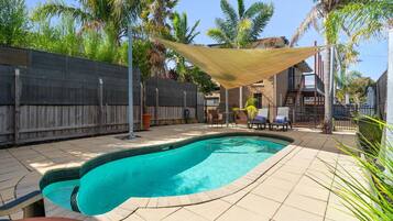A backyard with a swimming pool, patio furniture, and a wooden fence.