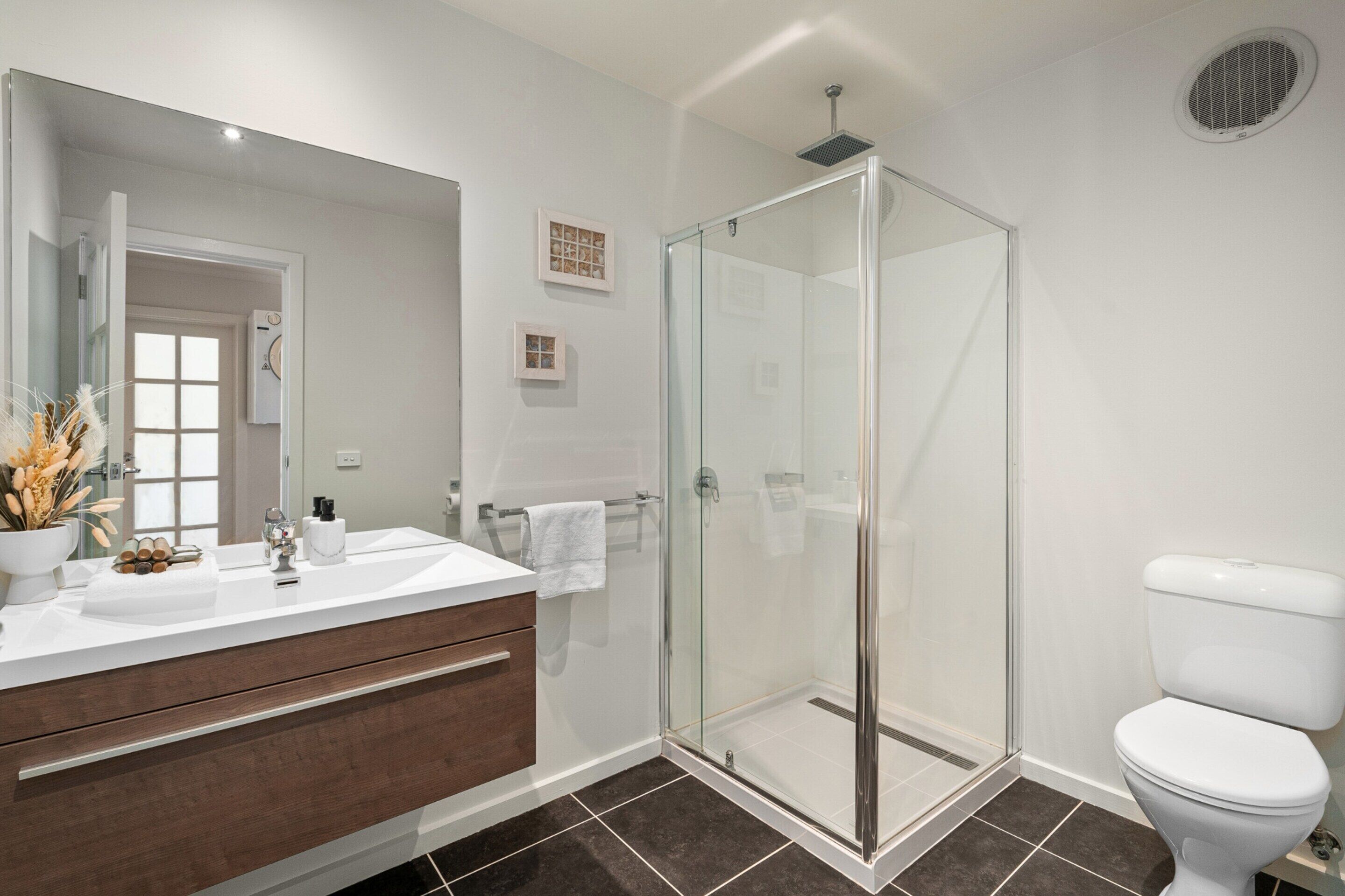 Un baño moderno con ducha de vidrio, inodoro blanco y tocador con espejo.