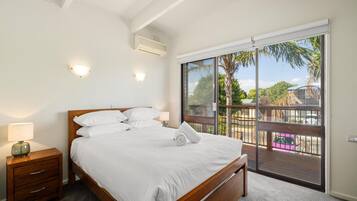 A bedroom with a large bed, a nightstand, a lamp, and a sliding glass door leading to a balcony.