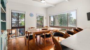A dining area with a wooden table and chairs, large windows, and a ceiling fan. - Spacious 4-bed Home 5-min From the Beach (Melbourne)