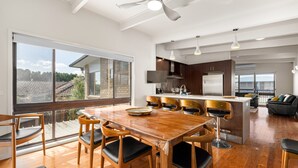 A spacious kitchen with a large island, wooden dining table, and chairs. There is a view of the outside through large windows. - Spacious 4-bed Home 5-min From the Beach (Melbourne)