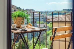 Ein Balkon mit Frühstückstisch, der mit Croissants und Kaffeetassen gedeckt ist, sowie eine Topfpflanze.
