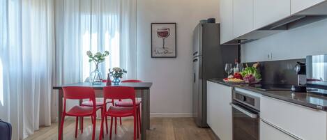 A modern kitchen with a dining area, featuring a table with red chairs, a refrigerator, and a stove.