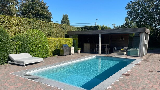A rectangular swimming pool with a brick patio, a lounge chair, and a covered seating area. - Holiday Home With Pool and Large Garden (Zwevegem)