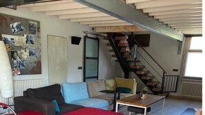 A spacious living area with a wooden floor, a red sofa, a blue sofa, a small table, and a staircase leading to an upper level. - Holiday Home With Pool and Large Garden (Zwevegem)