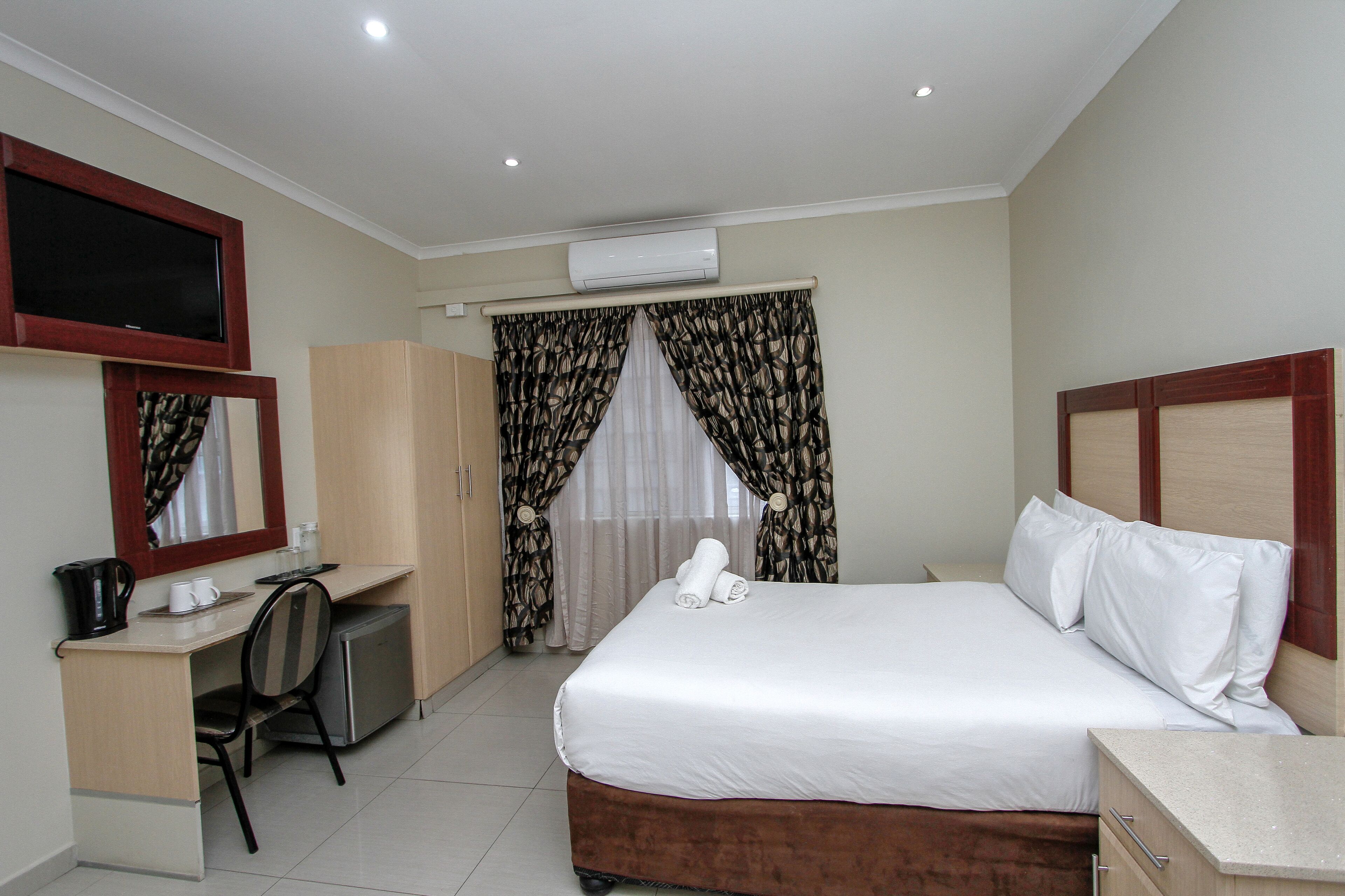 Habitación de hotel con cama, escritorio, silla, televisor y aire acondicionado.