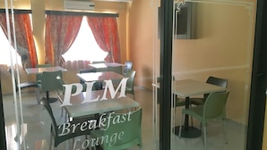 A breakfast lounge with tables and chairs, a large window with curtains, and an air conditioning unit on the ceiling. - PLM Palace Lodge (Durban)