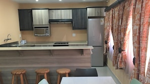 A modern kitchen with a built-in microwave, stove, and refrigerator. There are wooden stools and a table with chairs. - PLM Palace Lodge (Durban)