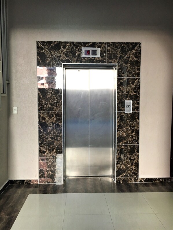 An elevator with a digital display showing the number 6, surrounded by marble walls and a tiled floor.