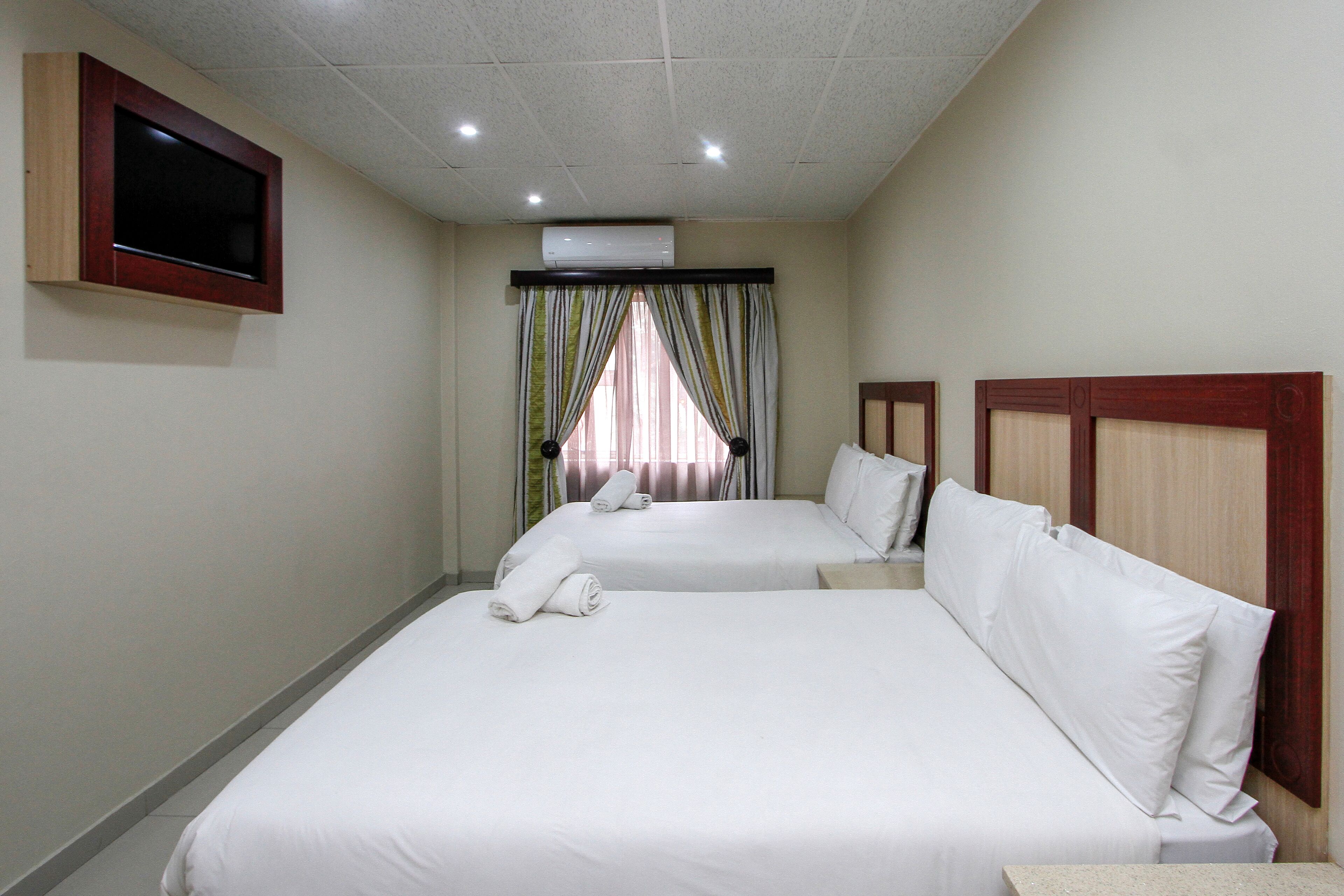 Habitación de hotel con dos camas, un televisor montado en la pared y un equipo de aire acondicionado sobre la ventana.