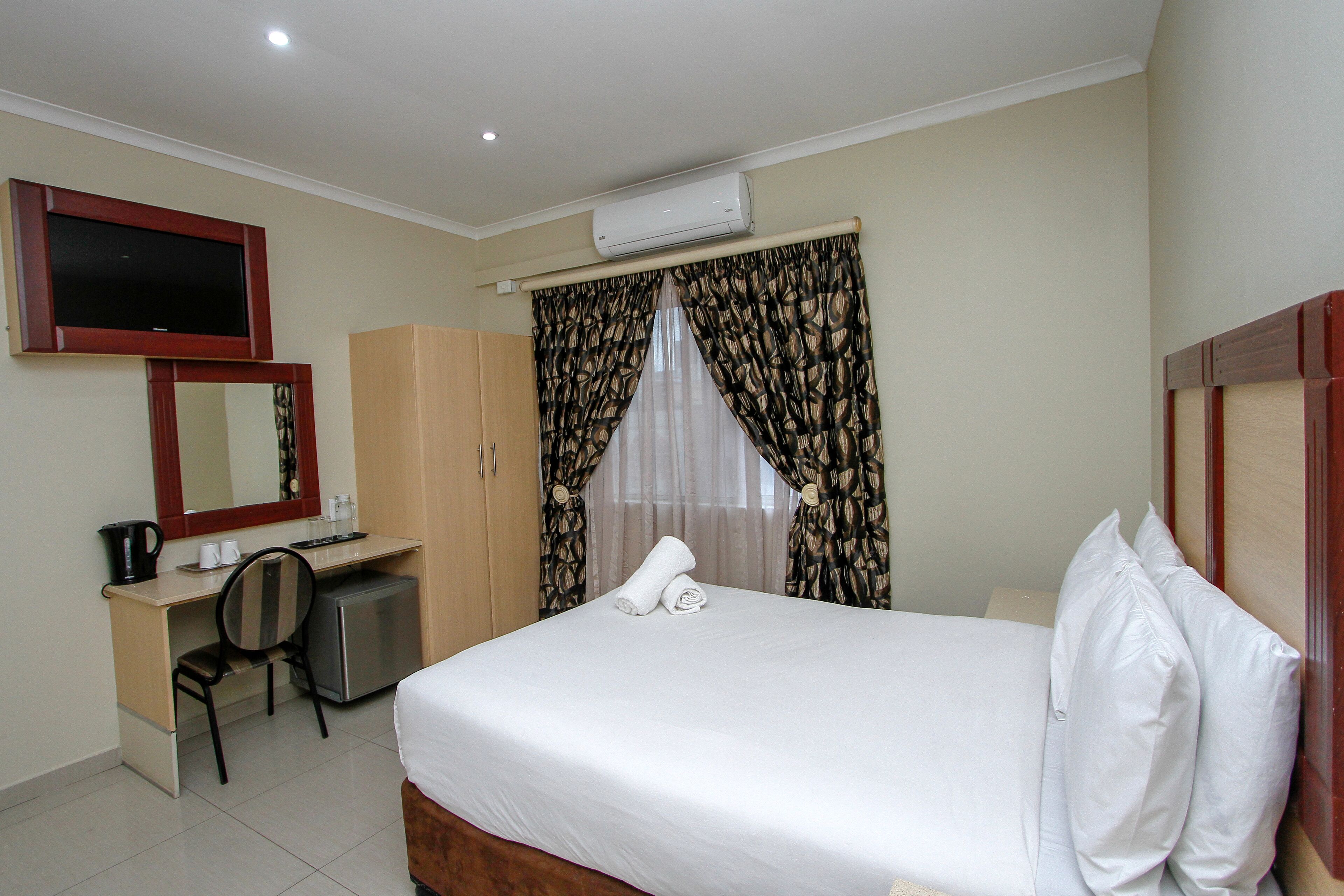 A hotel room with a bed, a desk, a chair, a television, and an air conditioning unit.