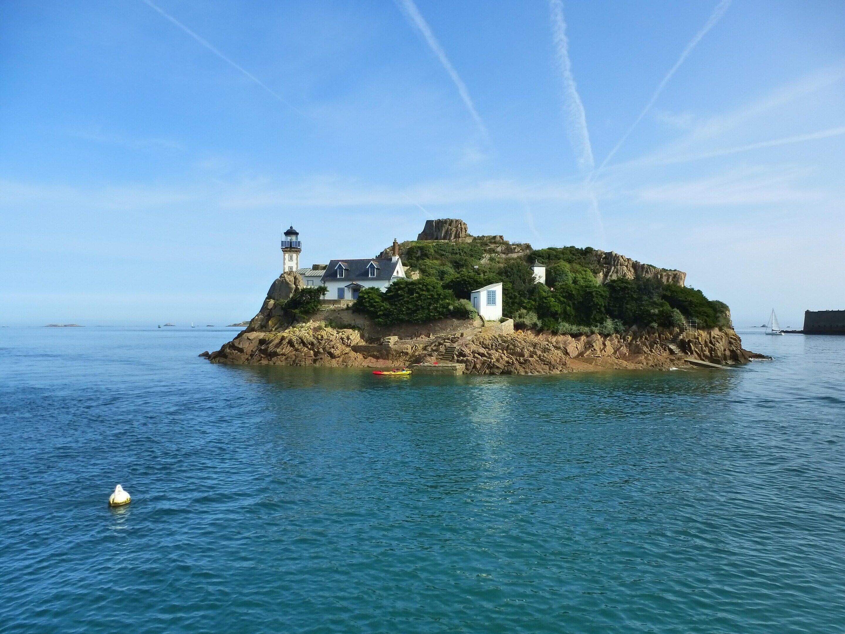 Un phare côtier situé sur une île rocheuse, avec un petit bâtiment et un bateau à quai.