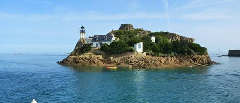 Un phare côtier situé sur une île rocheuse, avec un petit bâtiment et un bateau à quai.