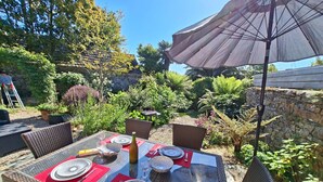 An outdoor dining area with wicker chairs, a glass table, and a large umbrella. - Granite Stone House - Guimaec (Guimaec)