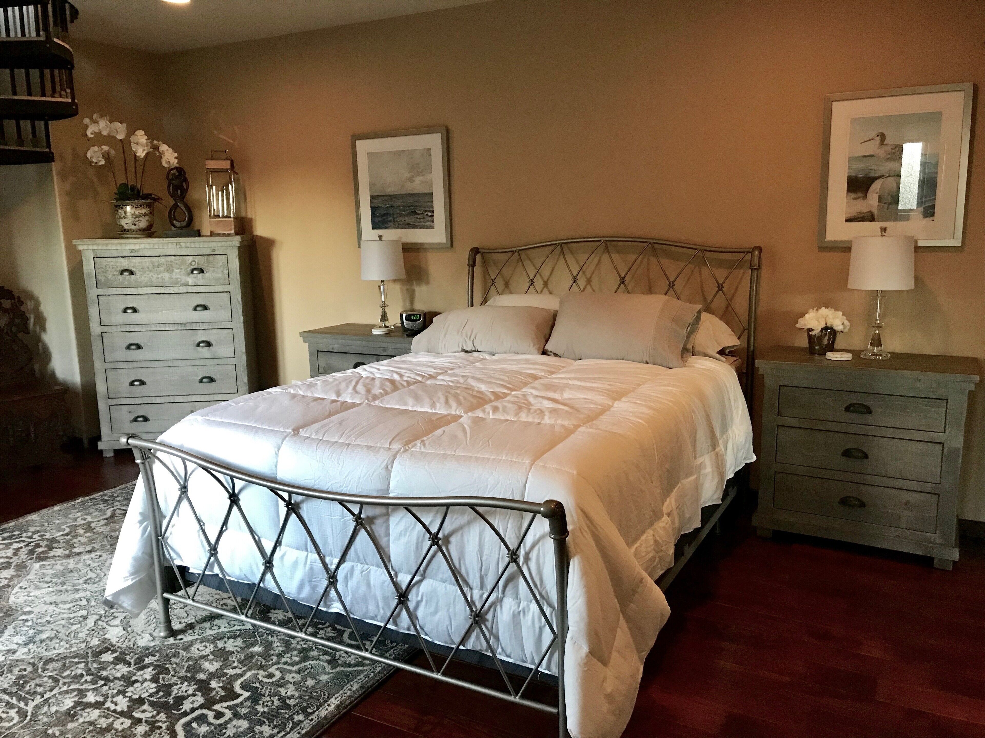 Een keurig opgemaakt slaapkamer met een groot bed, twee nachtkastjes, een dressoir en twee ingelijste foto's aan de wand.