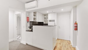 A compact kitchen with white cabinetry, a built-in stove, and a microwave. There is a fire extinguisher mounted on the wall. - Chic 1-bed Apartment Steps From Shopping Street (Melbourne)