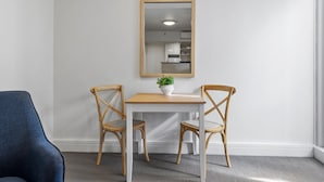 A room with a white table and two wooden chairs, a potted plant on the table, and a mirror on the wall. - Chic 1-bed Apartment Steps From Shopping Street (Melbourne)