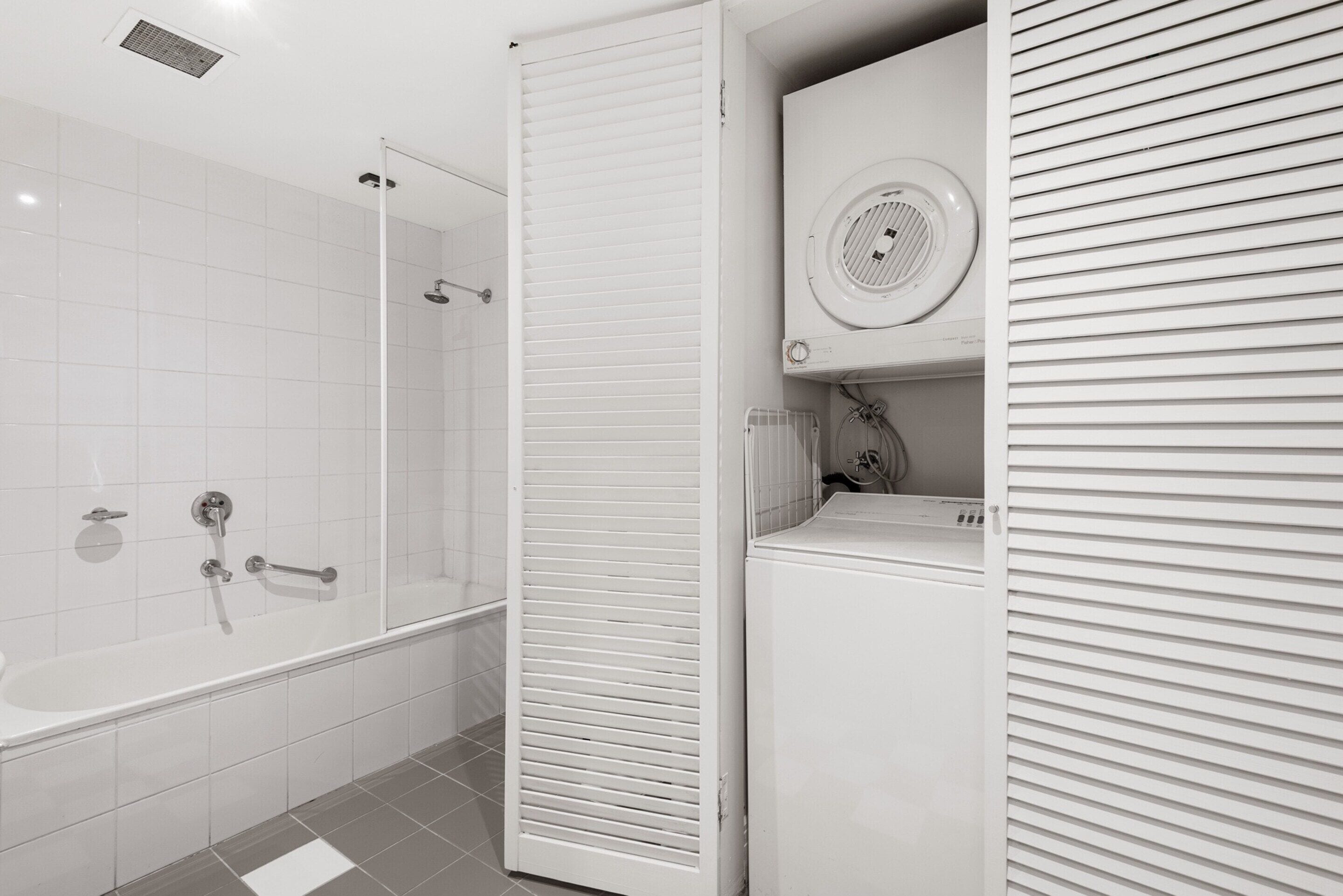 A modern bathroom with a glass-enclosed shower, a white bathtub, and a built-in washing machine.