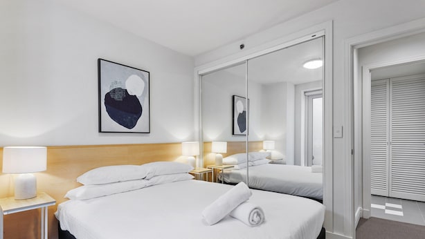 A hotel room with a large bed, a bedside table with a lamp, a mirror, and a framed artwork on the wall. - Chic 1-bed Apartment Steps From Shopping Street (Melbourne)