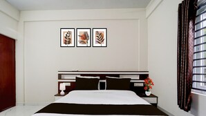 Un dormitorio con cama, mesita de noche, lámpara, ventana con cortinas y tres cuadros en la pared.