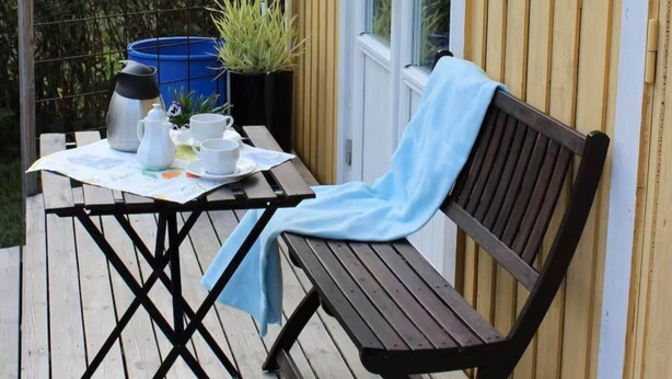 Een houten terras met een gedekte tafel voor thee, een bankje en plantenpotten.