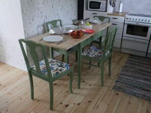 Un coin repas avec une table en bois, des chaises vertes et une cuisine en arrière-plan.