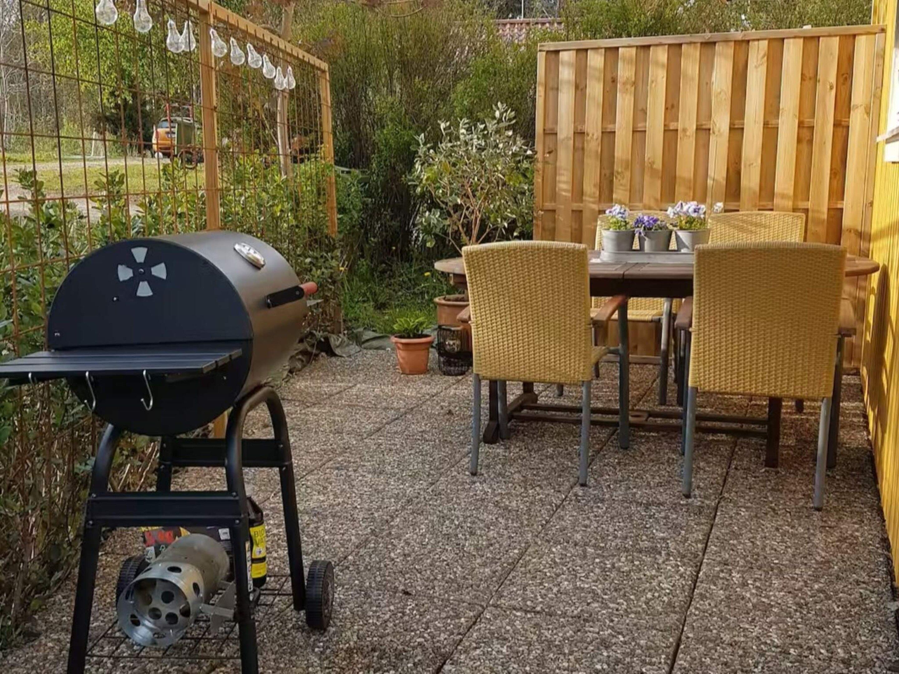 An outdoor patio with a grill, wicker chairs, and a wooden fence.