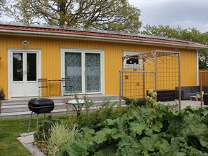 A yellow building with a red roof, a sliding glass door, a small window, and a garden area with plants. - 4 Person Holiday Home in Lur (Lur)
