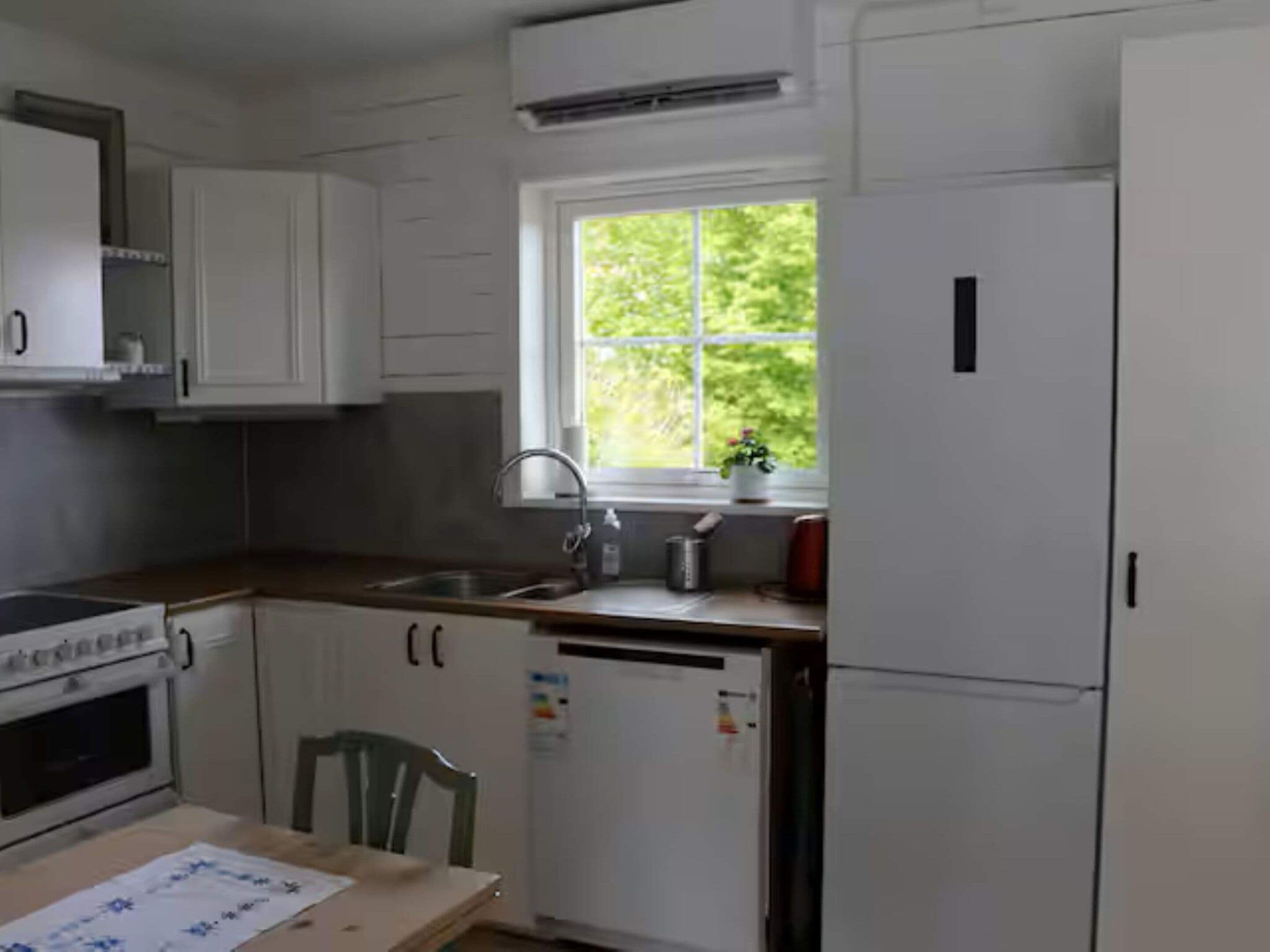Una cocina con armarios blancos, una ventana, un fregadero, una estufa y un refrigerador.