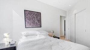 Een moderne slaapkamer met een groot bed, een nachtkastje met een lamp, een lijst met abstract kunstwerk en een kledingkast.