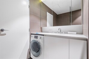 Une salle de bain moderne équipée d’un lave-linge intégré, d’un lavabo et d’un grand miroir.