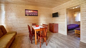 A wooden cabin interior with a dining table, chairs, a sofa, a TV, and a bedroom with beds. - Elegant House With Terrace Near Sea (Krokowa)