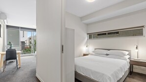 A modern bedroom with a large bed, bedside tables, a desk, and a view of the outside. - Fitzroy North 1-bed With Balcony by Edinburgh Park (Melbourne)