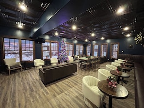 A spacious indoor area with a large Christmas tree, multiple seating arrangements, and large windows offering a view of a snowy landscape. - Ski-In/Ski-Out 1BR at Granby Ranch · Lift Steps Away (Granby)