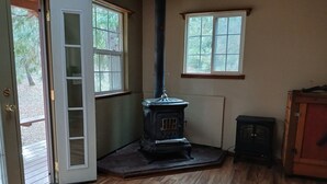 Quarto com lareira a lenha, porta para o exterior e janela com vista para árvores.
