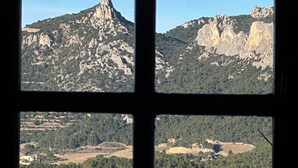 Vista dalla finestra su un paesaggio montuoso con cime rocciose e zone boschive.