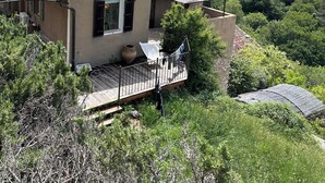 Una casa con tetto in tegole, un balcone e vista su una valle verdeggiante e colline boscose.