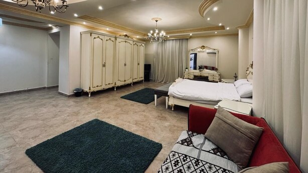 A spacious bedroom with a large bed, a red sofa, and a wardrobe. - فيلا للايجار اليومي خمس غرف مستقله (6 اكتوبر)