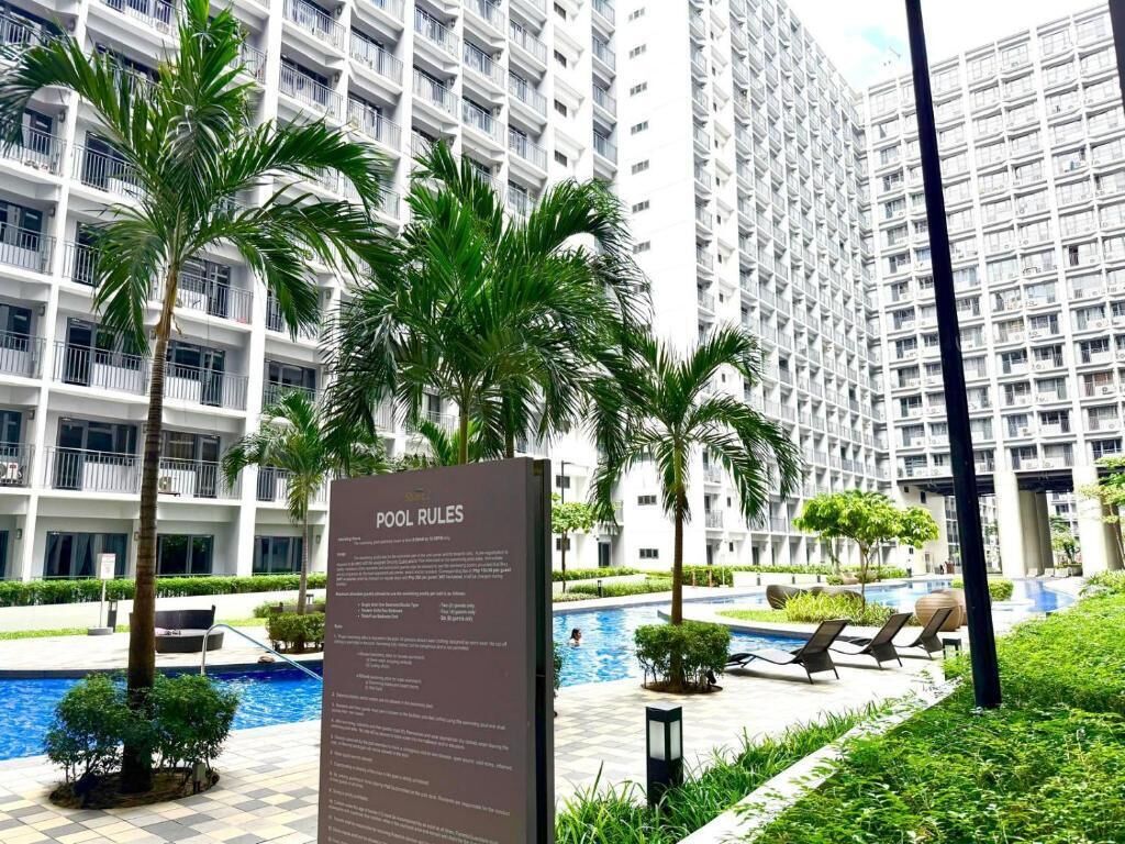 A pool area with a sign detailing pool rules, surrounded by palm trees and modern buildings.