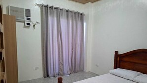 Ένα υπνοδωμάτιο με ένα ξύλινο κρεβάτι, μια γκρι κουρτίνα και ένα κλιματιστικό που είναι τοποθετημένο στον τοίχο.