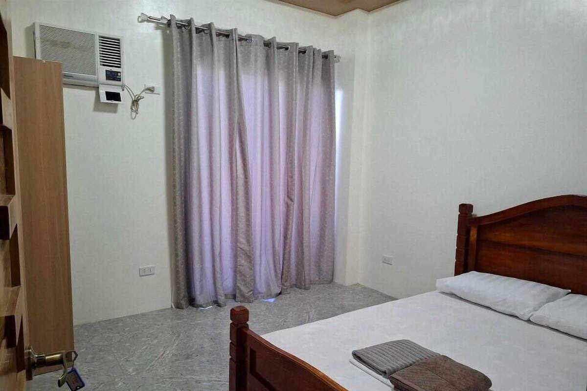 A bedroom with a wooden bed, a grey curtain, and a wall-mounted air conditioner.