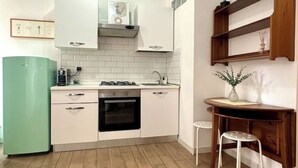 Eine kleine Küche mit weißen Schränken, einem grünen Kühlschrank, einem Herd und einem Essbereich mit Hocker.