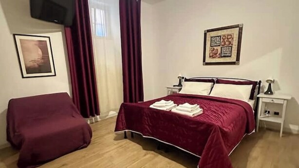 Ein Hotelzimmer mit einem Bett, einem Sessel, einem Nachttisch, einem Fernseher und einem gerahmten Bild an der Wand.