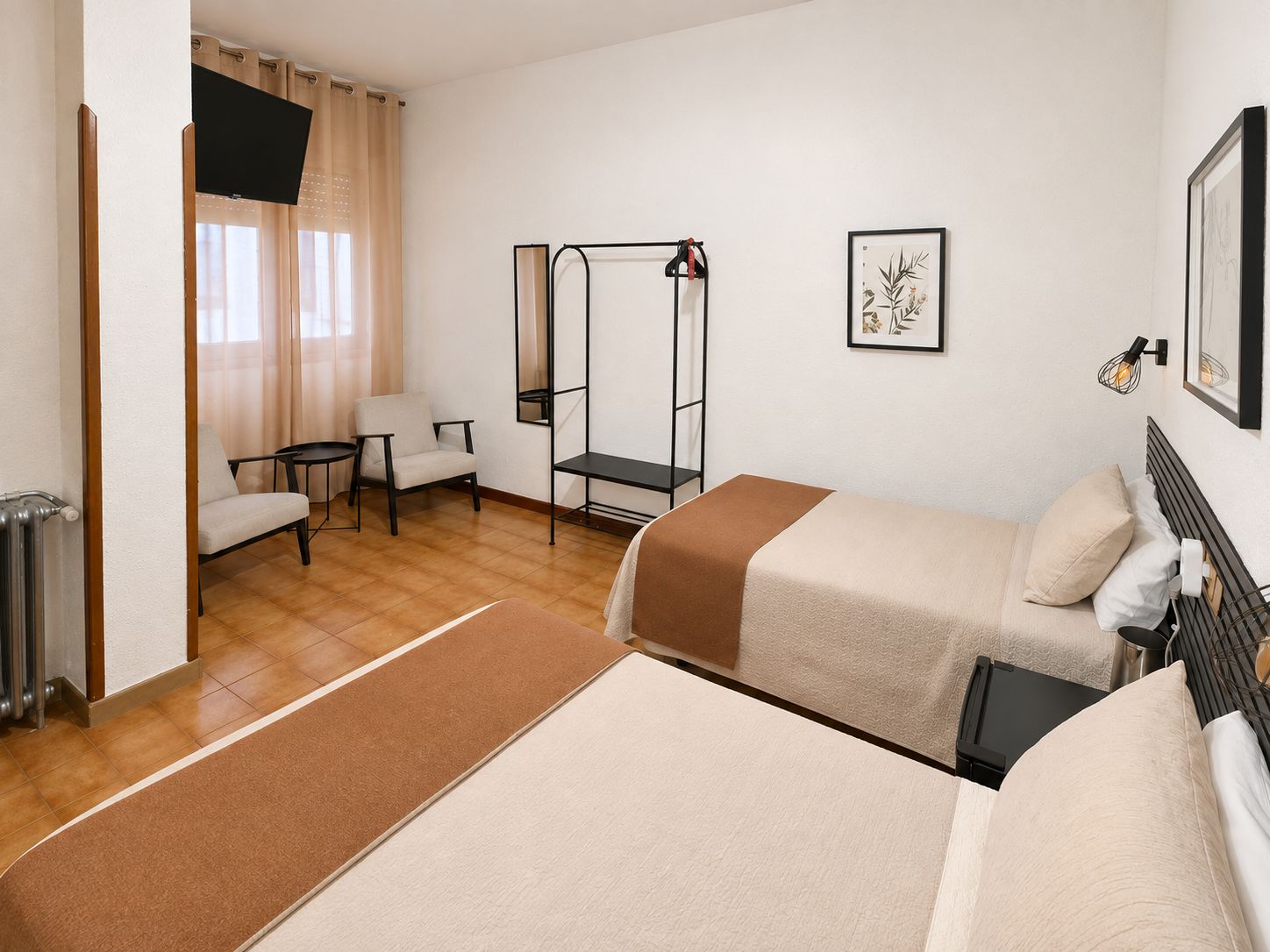 A hotel room with two beds, a chair, a small table, a TV, and a framed picture on the wall.
