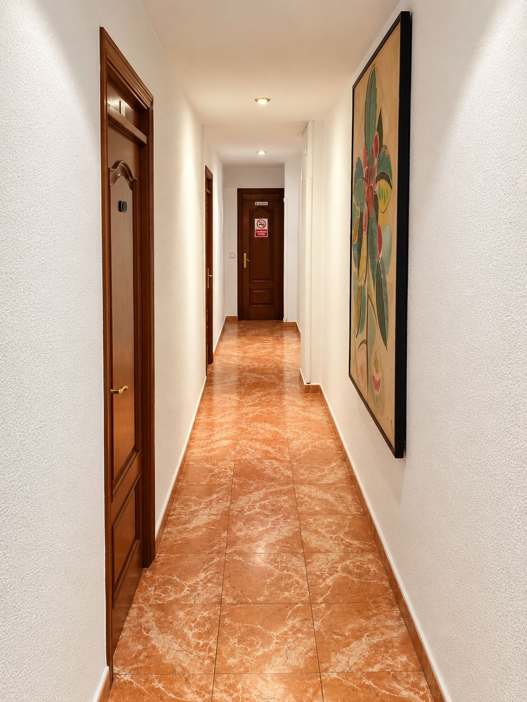 Un pasillo con suelo de mármol, puertas de madera y un cuadro en la pared.