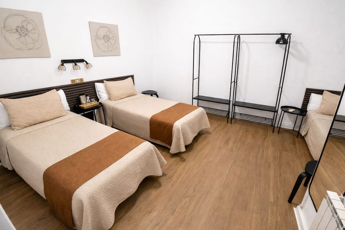 A hotel room with two beds, a small table, a chair, and a large window.