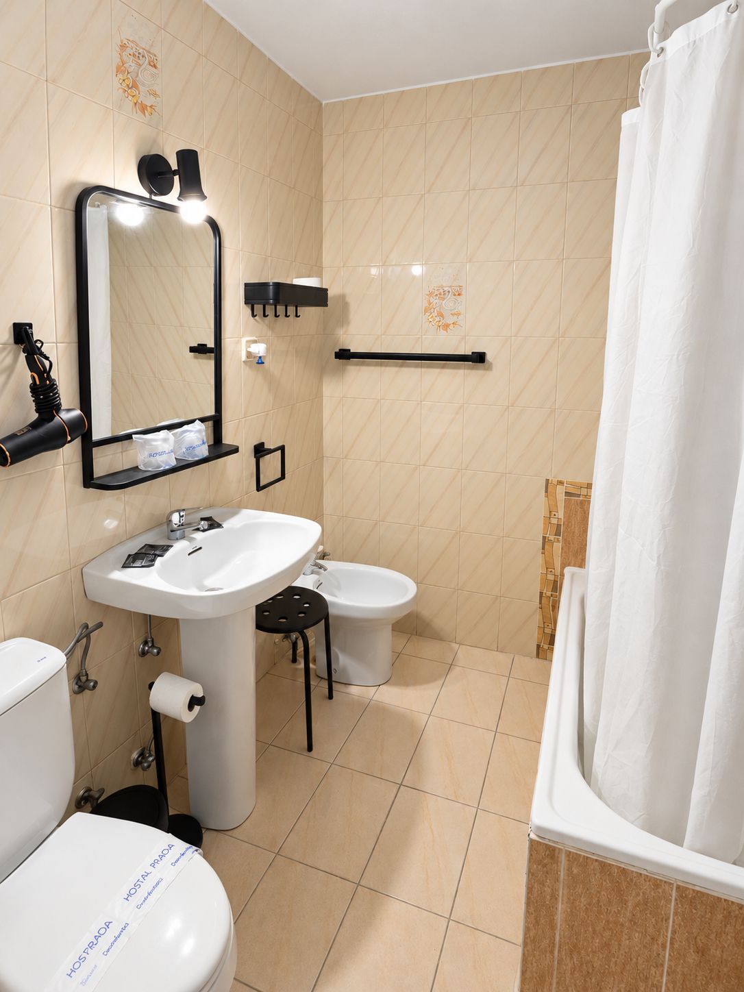 A bathroom with a white sink, a toilet, a bidet, a mirror with lights, a towel rack, and a shower curtain.