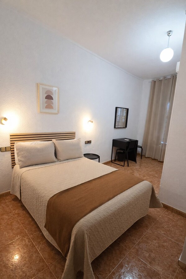 Un dormitorio ordenado con cama, mesitas de noche, escritorio y silla.